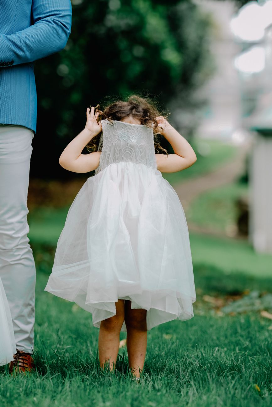 Shy young girl hiding her face in her dress next to a parent