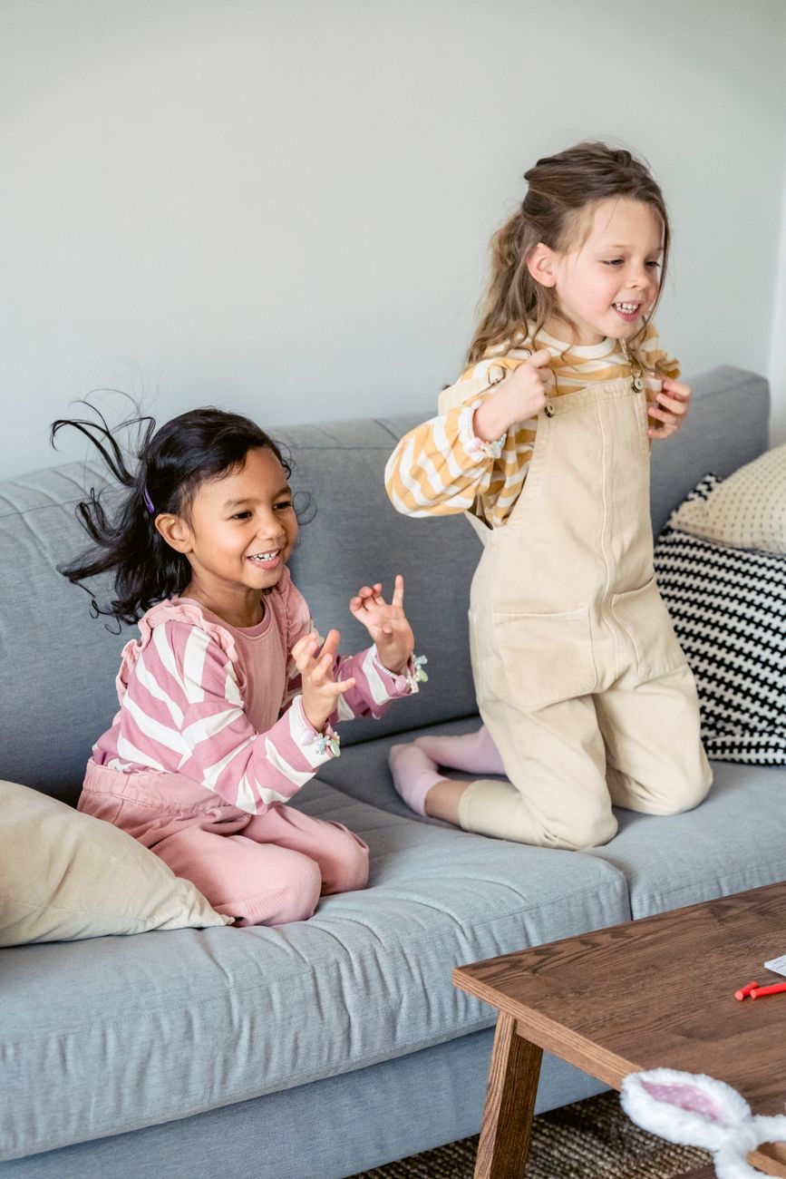 Two energetic young girls jumping and laughing on a sofa